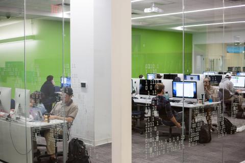 four rows of desks with students working, against a green back wall