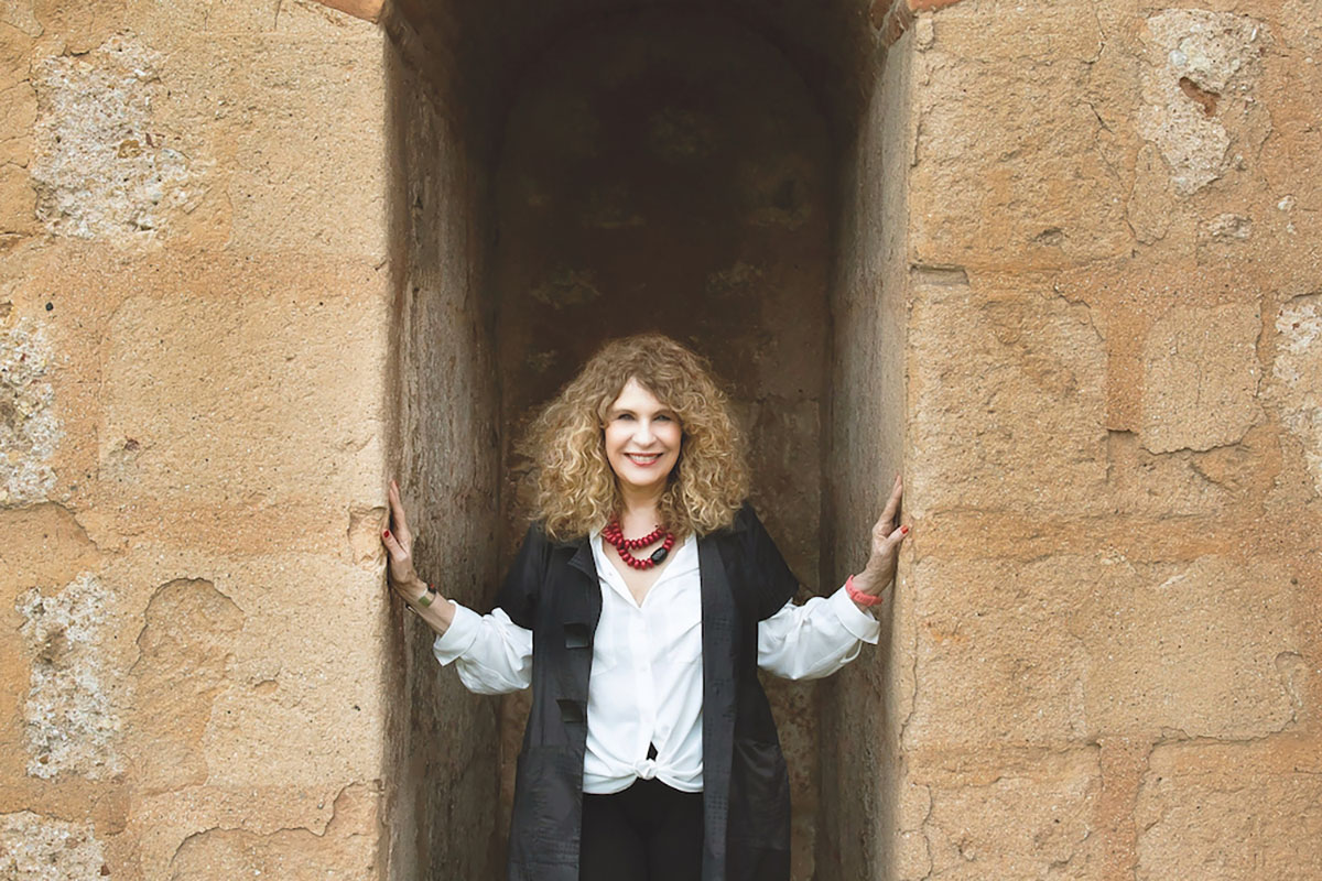 Gioconda Belli standing between stone walls with hands pressed outwards against them.