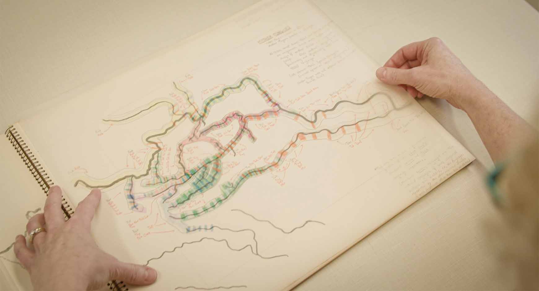 Handrawn map with locations of indigenous language hotspots with translucent overlay of key data, framed by pair of hands laying down overlay.