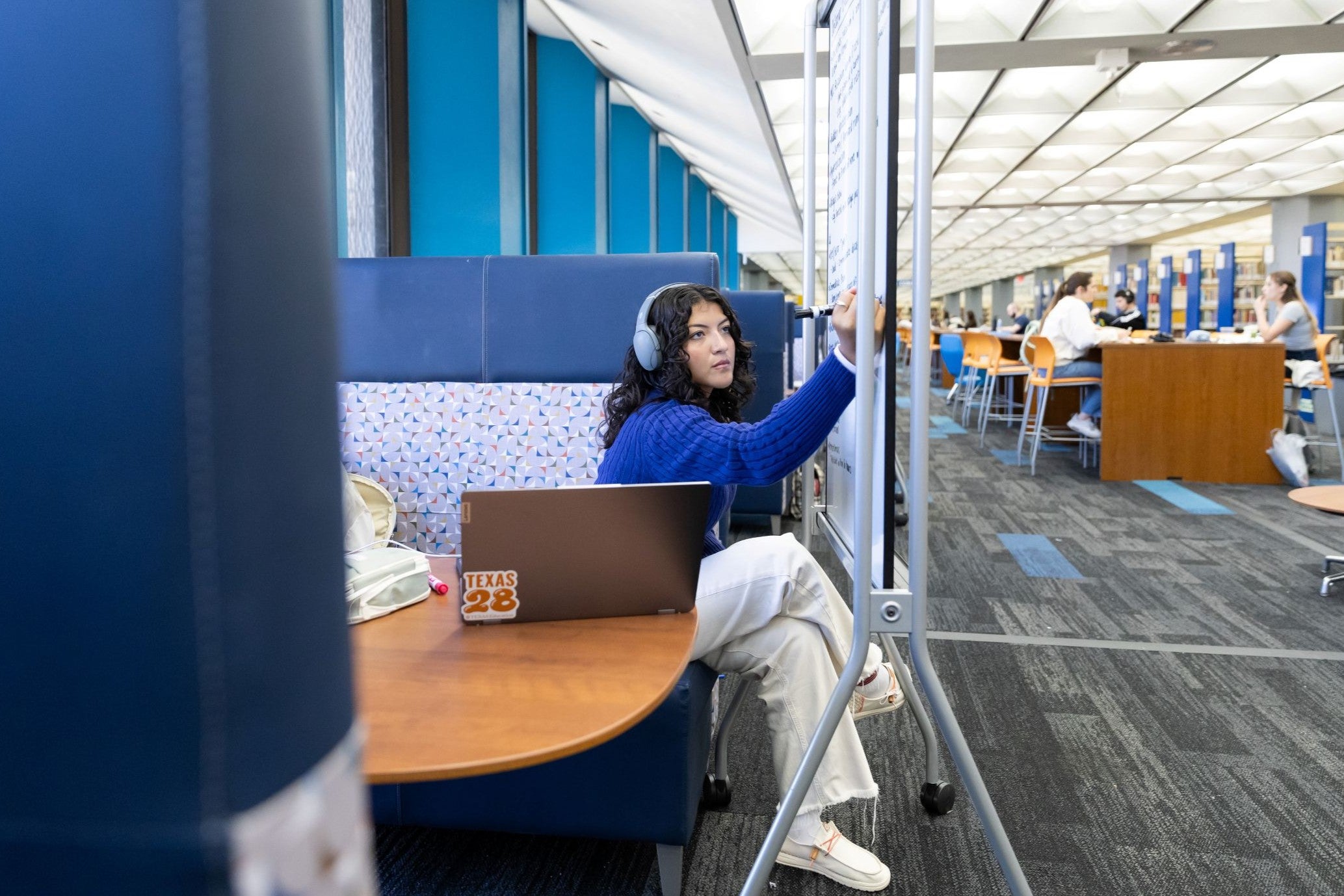 a student with curly black hair and headphones writes on a whiteboard.