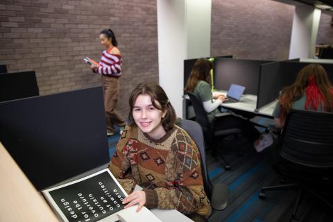 student at a study carrell, looking up at the camera and smiling