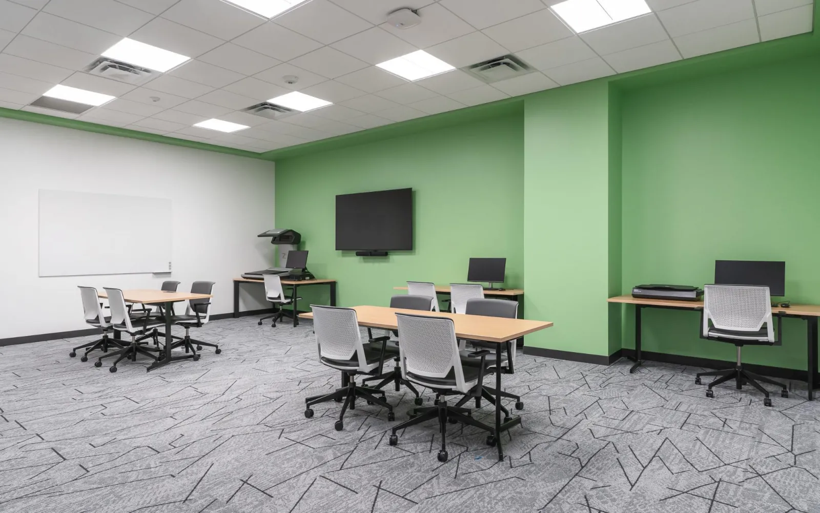 Alt text for image: Two small four person tables are floating in the middle of the room, with a one person table with an overhead scanner located in the back left corner. To the right of the overhead scanner there is a TV, and then two one person tables each equipped with a flatbed scanner.