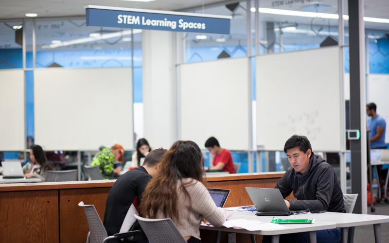 Three students sitting at a table together looking at their laptops in the UFCU Room